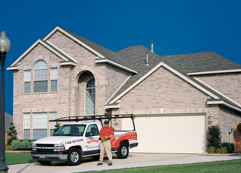 Garage Door Repair Technician standing in front of a white garage door on two-story white brick home