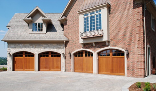 Four wood-grain carriage-style garage doors with round tops on a large brick home.