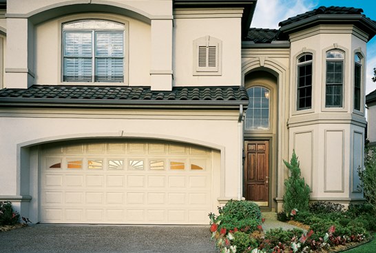 White steel garage door with slightly arched top and small windows in the top, in home with white stucco siding.