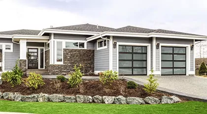 Modern garage door on a residential home. The garage door is black aluminum, with glass panels. 